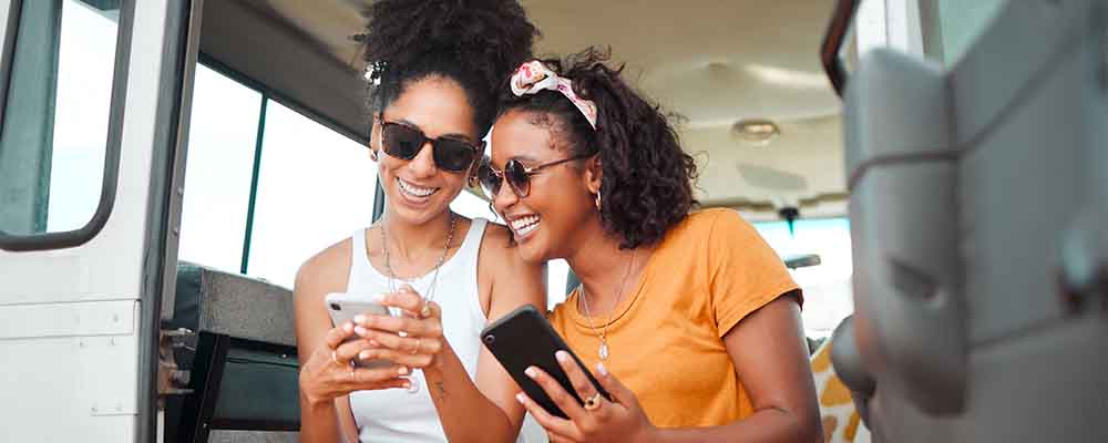 Black friends, phone and social media travel in communication together for road trip adventure. Happy and excited African American women sharing moments of traveling on mobile smartphone for vacation