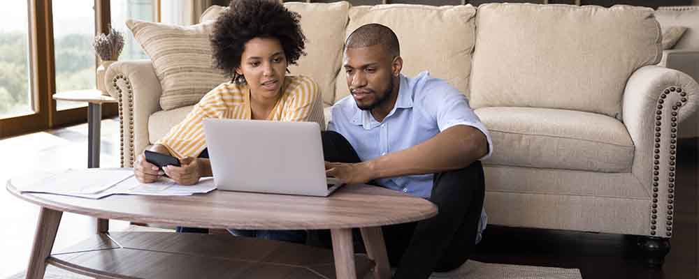 African couple sit in living room discuss receipts, control family budget, calculate household bills to pay, utility expenses, make payment via e-bank app on laptop, accounting, money control concept